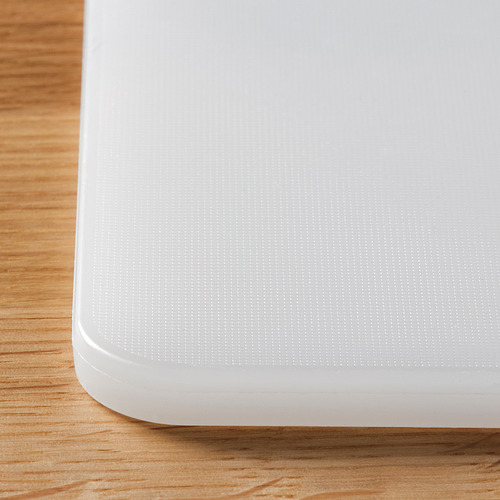 Primer plano de una tabla de cortar de plástico limpia, blanca y texturizada sobre una superficie de madera, que muestra su calidad suave, uniforme y duradera.
