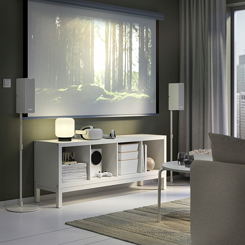 Sala de estar moderna con estante KALLAX, parlantes y escena del bosque en pantalla grande, sofá gris, mesa de café.
