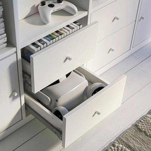 Mueble de tv KALLAX blanco con cajón abierto para guardar consolas de juegos, y estante superior con estuches de juegos y un control remoto.