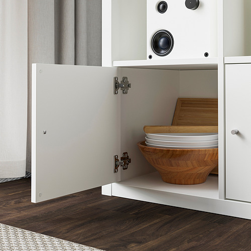Armario blanco abierto que muestra el cuenco de madera, los platos y la tabla de cortar almacenados en el interior, con el suelo de madera oscura visible.