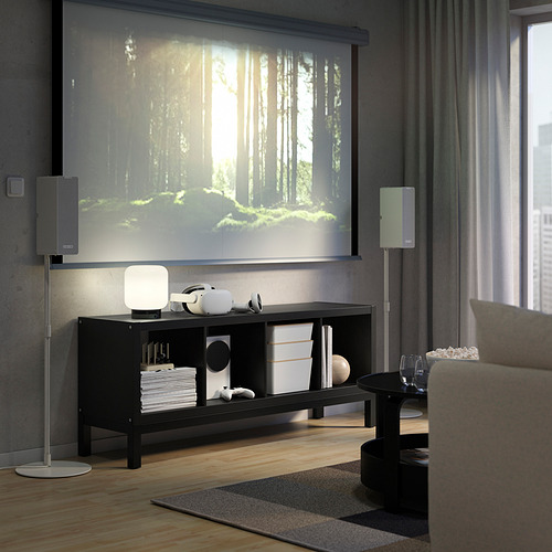 Sala de estar moderna con estante KALLAX, parlantes y televisor que muestra un bosque, sofá marrón, bocadillos y vino.