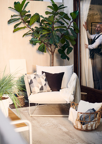 Sala de estar moderna con sofá HAVSTEN blanco, almohadas estampadas, gran planta verde y cesta con toallas.