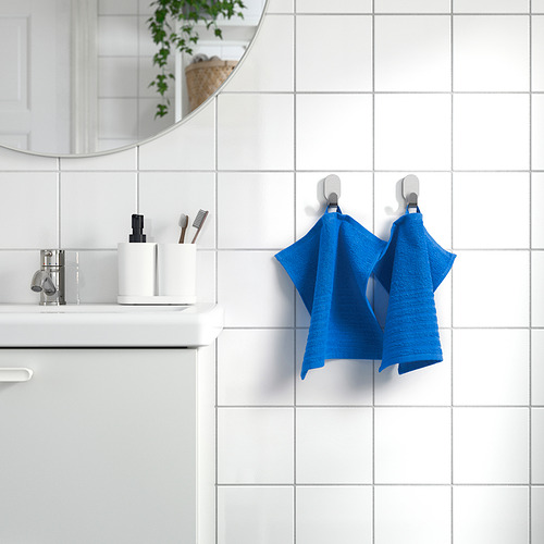 Baño moderno con toallas VÅGSJÖN azules en ganchos, espejo sobre lavabo con artículos de tocador.
