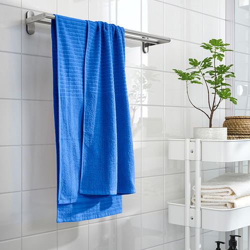 La toalla azul brillante cuelga de un estante de pared, junto a estantes blancos con toallas dobladas y una planta.