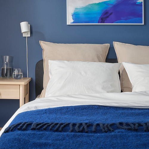 Dormitorio moderno con cama grande, pared azul y arte abstracto. Almohada GURLI, beige claro, fundas visibles. Dos vasos al lado de la cama.