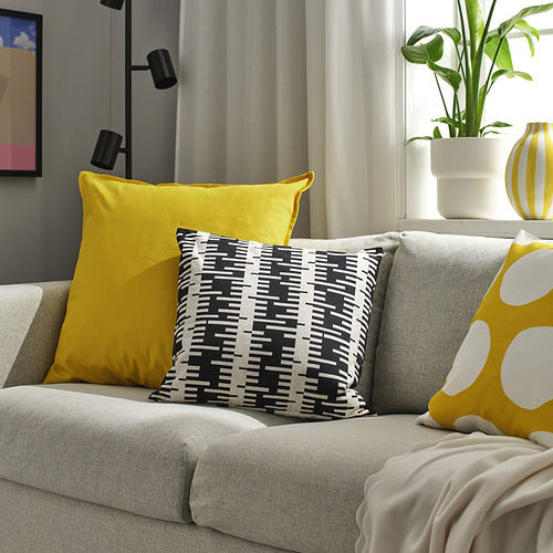 Escena de sala de estar con sofá gris, que muestra grandes cojines amarillos, estampados y de lunares. Planta y decoración en las inmediaciones.