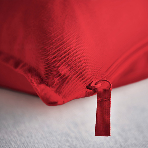 Funda de cojín roja en la cama, se muestra detalle de cremallera, tejido de alta calidad.