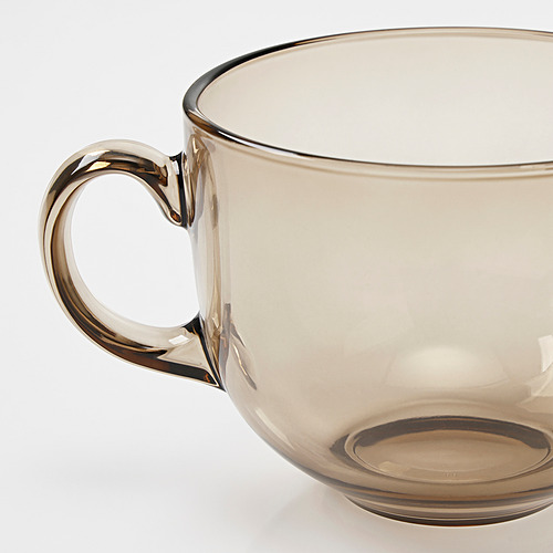 Taza de cristal color ámbar con un mango robusto y elegantemente curvado, que refleja la luz y muestra su acabado claro y suave.