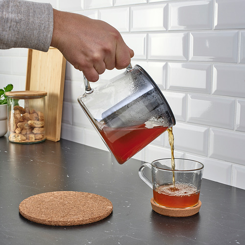 La persona vierte té de una tetera RIKLIG de vidrio con un infusor en una taza en el mostrador de la cocina.