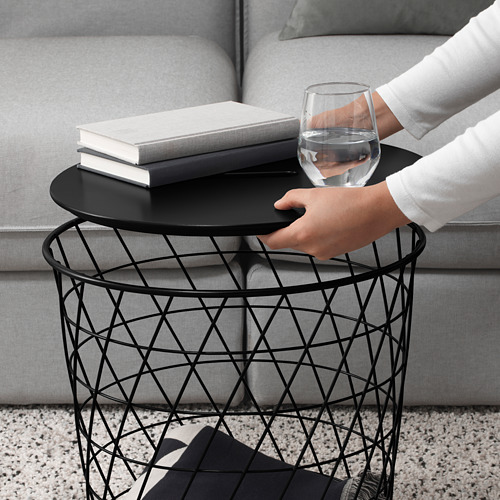 Una persona sosteniendo una moderna mesa auxiliar de metal con un vaso de agua y libros, mostrando su portabilidad y funcionalidad de almacenamiento.