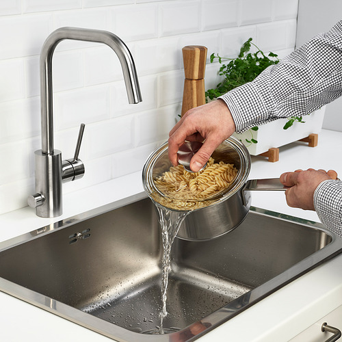 Persona escurriendo pasta en el fregadero de la cocina con grifo de plata moderno.