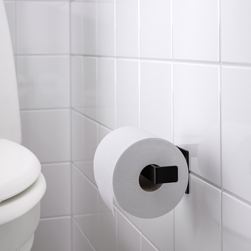 Soporte de papel higiénico negro montado en una pared de azulejos blancos, sosteniendo un rollo de papel higiénico blanco, cerca de un inodoro blanco.