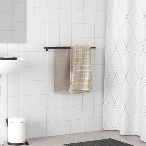 El toallero SKOGSVIKEN negro sostiene las toallas cerca de la pared de azulejos blancos. Es delgado, horizontal, cabe entre artículos más grandes.