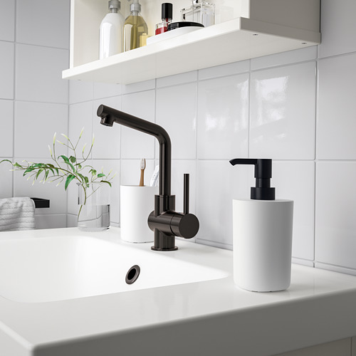 Lavabo de baño moderno con grifería negra STORAVAN y accesorios blancos. Dispensador de bomba, soporte para cepillo de dientes y bandeja sobre encimera blanca limpia.
