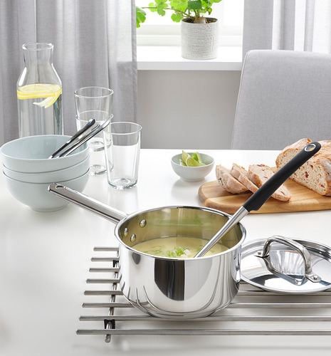 Cocina moderna con cacerola de sopa en salvamanteles, tazones, vasos, jarra, silla y planta junto a la ventana.