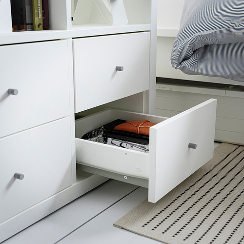 Cómoda blanca abierta con una carpeta naranja y un folleto en blanco y negro en el interior. Parte de la solución de almacenamiento KALLAX.