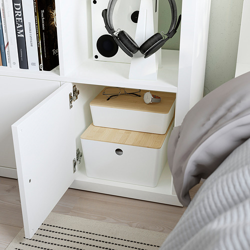 Estante KALLAX junto a la cama con cajas y auriculares, que muestra almacenamiento y organización.