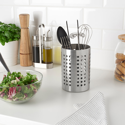 Escena de cocina moderna con portautensilios de acero inoxidable relleno de utensilios de cocina, junto a un plato de ensalada y hierbas.
