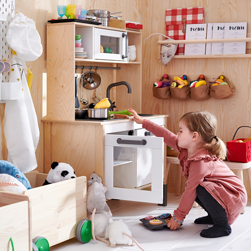 Niño jugando con cocina de madera y juguetes.