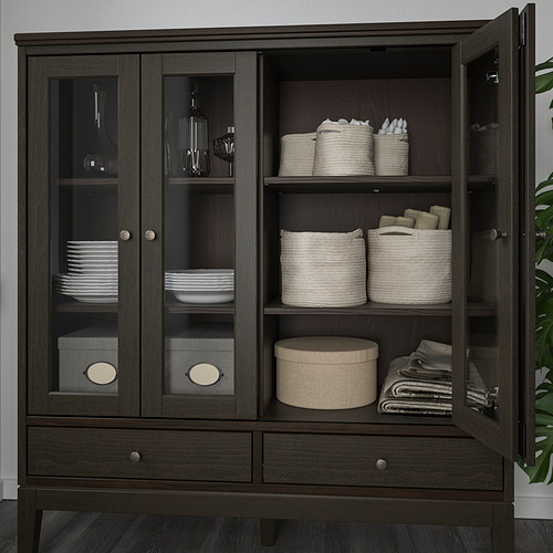 Armario de madera oscura con puertas de cristal que muestra platos, cubiertos y cestas de almacenamiento de telas.