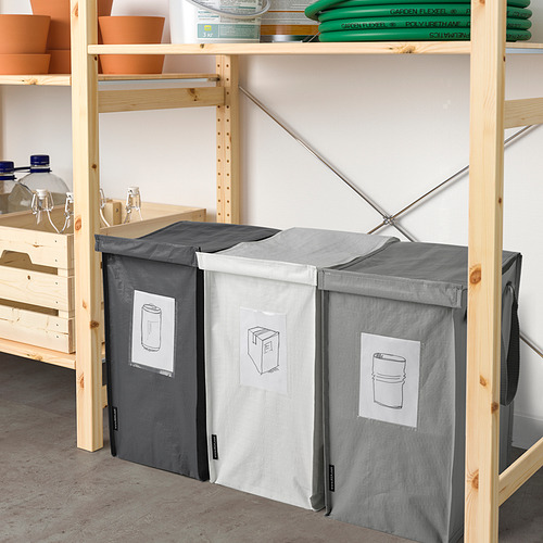 Tres grandes bolsas de reciclaje DIMPA grises en estantes, cada una con un asa y un bolsillo etiquetado, cuidadosamente organizadas.