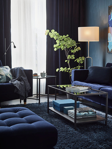 Sala de estar moderna con muebles azul oscuro, lámpara plateada, mesa de vidrio y alfombra azul.