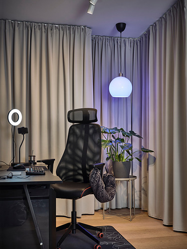 Oficina en casa negra con escritorio, lámpara, silla, anillo de luz, planta, cortinas grises.