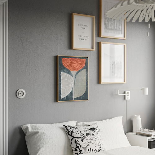 Dormitorio moderno con colorido póster BLODFLÄDER. Tres láminas enmarcadas en pared gris, cama con almohadas blancas, lámpara colgante.