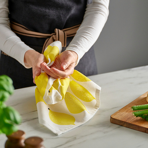 La persona envuelve un paño de cocina con forma de limón, probablemente para secar las manos o los platos, con artículos de cocina y plantas cerca.