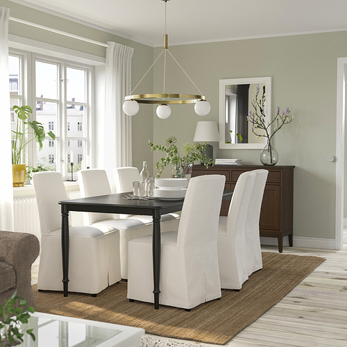 Comedor moderno con lámpara colgante de latón, globos de vidrio, sillas blancas, pared verde, plantas, piso de madera.