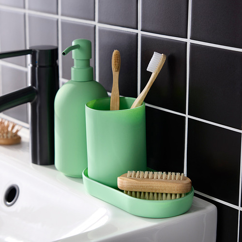 Dispensador de jabón de vidrio verde, soporte para cepillos de dientes y bandeja en fregadero blanco. Fondo de pared de azulejos en blanco y negro.