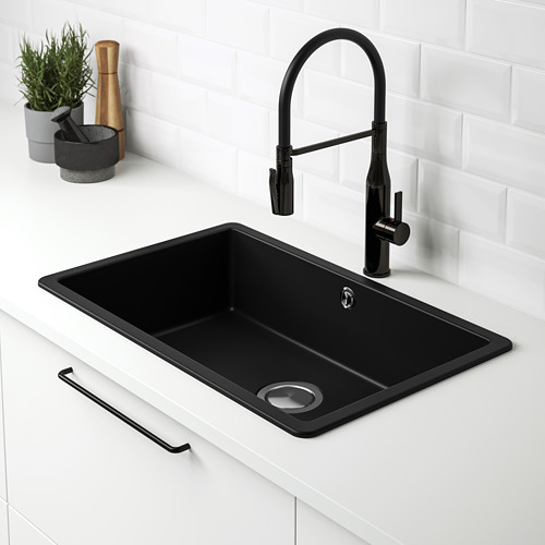 Fregadero de cuarzo KILSVIKEN negro con grifo desplegable, ubicado en una encimera blanca contra un protector contra salpicaduras de azulejos blancos.