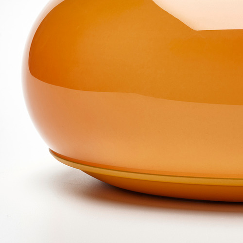 Elegante lámpara de cristal naranja con acabado liso que proyecta un cálido resplandor. Diseño moderno y minimalista, probablemente de mesa o de pared.