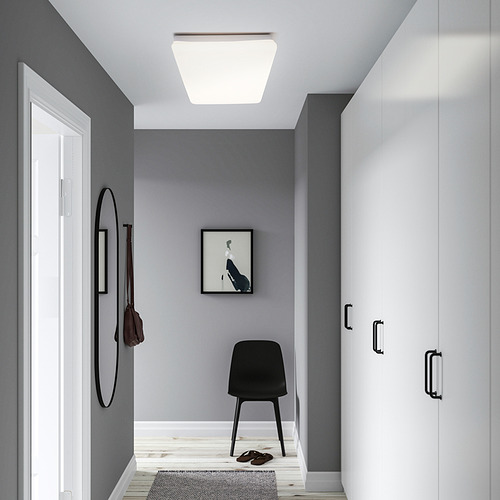 Entrada moderna con panel de luz JETSTRÖM, armario blanco, silla negra, espejo y felpudo.