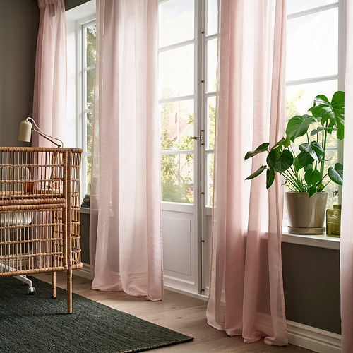 Habitación luminosa con cortinas transparentes rosas STENFRÖ, una silla alta de mimbre y una planta verde en el alféizar de una ventana.