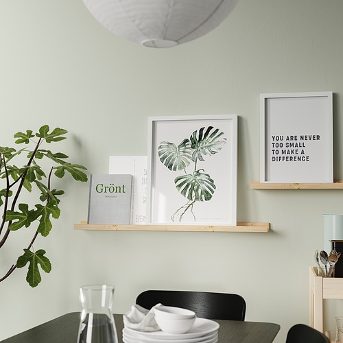 Un comedor moderno, una estantería de madera que muestra obras de arte enmarcadas, libros y una planta. A continuación se coloca una mesa con tazas y platos.