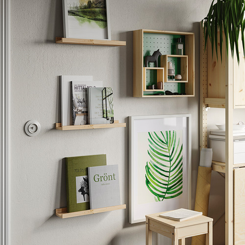 Las estanterías de madera de NORDHÄGG contienen libros, plantas y obras de arte. Diseño limpio y lineal en una pared clara con vegetación.