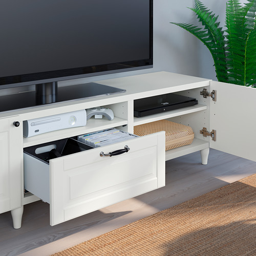 Mueble de TV blanco con cajón deslizante, consola de juegos, control remoto y DVD. Almacena y organiza dispositivos multimedia y cables.