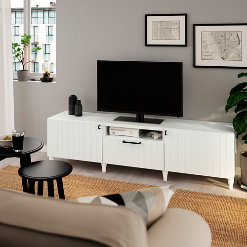 Sala de estar moderna con mueble de TV SUTTERVIKEN blanco, pantalla plana y sofá beige. Mapas decorativos y plantas alrededor.