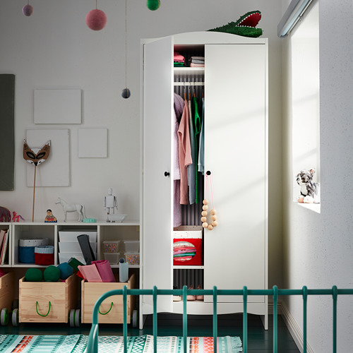 Habitación infantil con mueble de almacenamiento SMÅGÖRA blanco abierto, donde se exhibe ropa y juguetes. Barandilla verde en primer plano.
