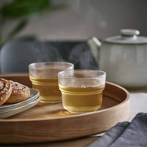 Dos vasos de té en bandeja de madera, humeante, con una tetera.