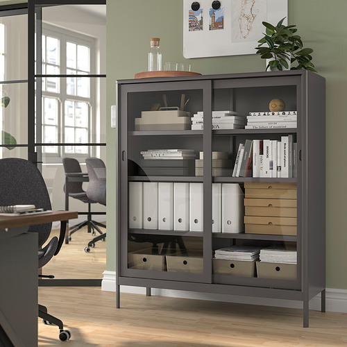 Armario de almacenamiento negro IDÅSEN con puertas de cristal en la oficina, donde se guardan libros y decoración, ahorra espacio.