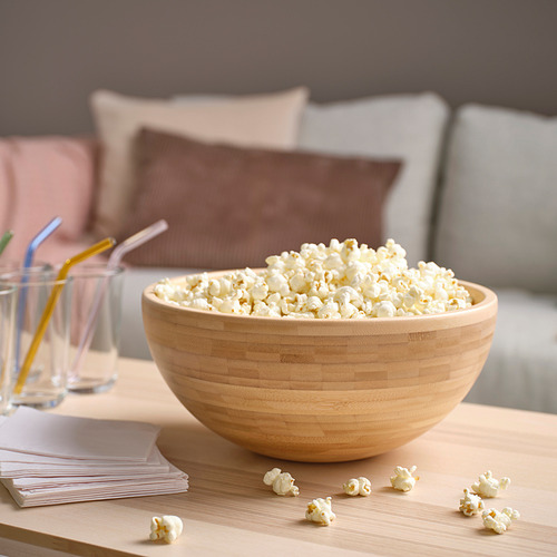 Un gran cuenco de madera lleno de palomitas de maíz se encuentra en una mesa de café cerca de vasos y cojines.