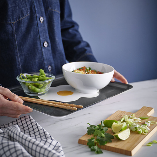 Persona que sostiene palillos cerca de la bandeja con tazón, edamame y tabla de cortar con lima y hierbas.