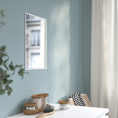 Espejo rectangular transparente con bordes ondulados en pared azul claro. En la cómoda, un cepillo, frascos y una planta. Fácil de colgar con cinta adhesiva.