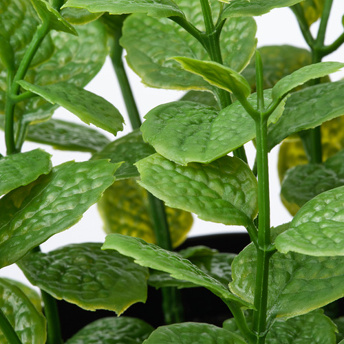 Primer plano de hojas verdes vibrantes y realistas de una planta artificial en maceta.