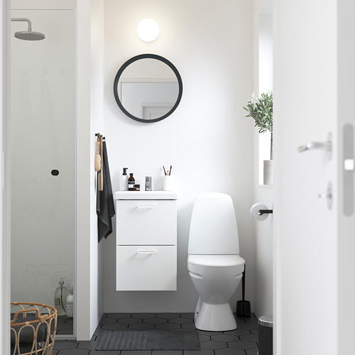 Baño moderno: lavabo blanco, espejo, inodoro, piso negro, alfombra gris, puerta blanca, decoración sencilla.