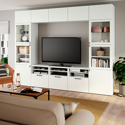 Sala de estar moderna con gran mueble de TV blanco BESTÅ y pantalla plana. Suelo de madera clara, sofá beige, mesa de centro con decoración. Planta derecha, ventana izquierda.