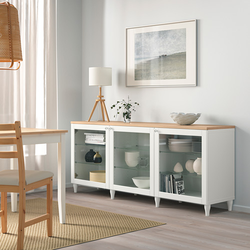 Aparador blanco OSTVIK con puertas de cristal, almacenamiento de platos y jarrones, en un ambiente de comedor minimalista.