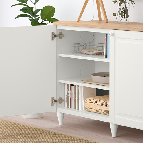 Un aparador blanco BESTÅ con puertas abiertas que deja ver estantes que contienen cestas y libros, mostrando su almacenamiento y organización.